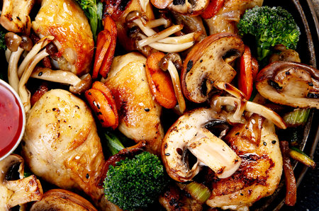 Chicken thighs baked with mushrooms, carrots and broccoli in a frying pan on a dark background. Top view.の写真素材