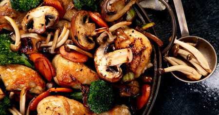 Chicken thighs baked with mushrooms, carrots and broccoli in a frying pan on a dark background. Top view.の写真素材