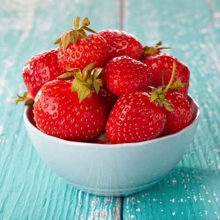 Bowl of fresh strawberries on blue wooden backgroundの写真素材