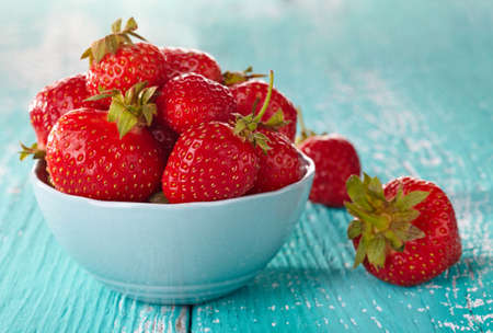 Bowl of fresh strawberries on blue wooden backgroundの写真素材