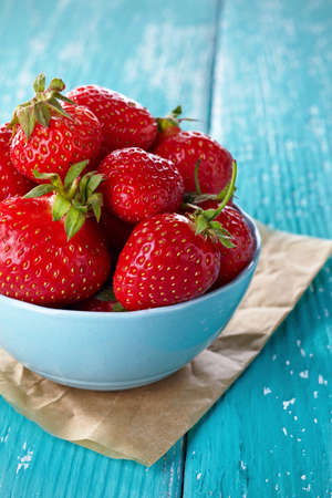 Bowl of fresh strawberries on blue wooden backgroundの写真素材