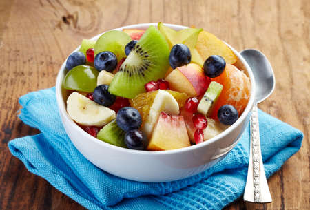 White bowl of fresh healthy fruit salad on wooden background