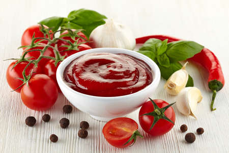 Bowl of tomato sauce with fresh ingredients on white wooden の写真素材