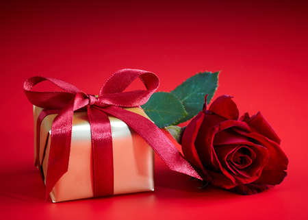 Golden gift box and red rose on red backgroundの写真素材