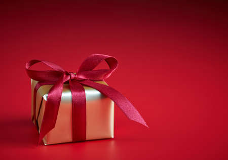 Golden gift box with red ribbon on red backgroundの写真素材