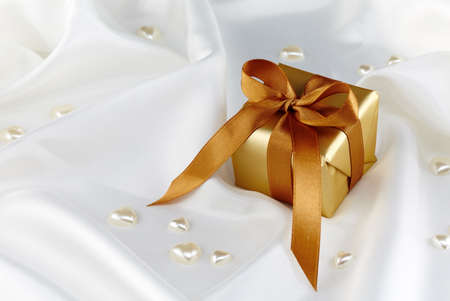 Golden gift box and pearl hearts on white satin fabricの写真素材