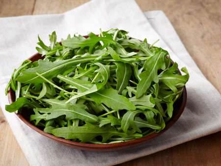 Bowl of fresh arugula leaves on wooden backgroundの写真素材