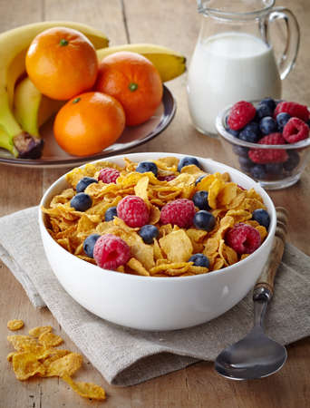 Bowl of corn flakes and fresh berries, jug of milk and fresh fruits on wooden backgroundの写真素材