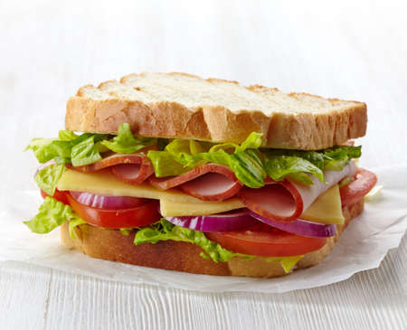 Sandwich with ham, cheese and fresh vegetables on white baking paperの写真素材