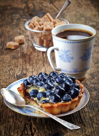 Plate of blueberry tart and cup of coffee on wooden backgroundの写真素材