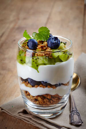 Healthy layered dessert with cream, muesli, kiwi and blueberries on wooden backgroundの写真素材