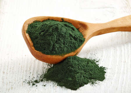 Wooden spoon of spirulina algae powder on white wooden backgroundの写真素材