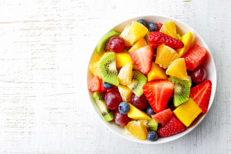 Bowl of healthy fresh fruit salad on wooden background. Top view.