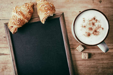 Blank blackboard with croissants and cup of coffee on wooden backgroundの写真素材