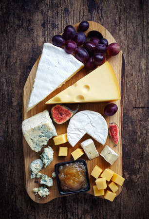 Cheese plate served with grapes, jam and figs on a wooden backgroundの写真素材