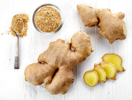 Fresh sliced ginger root and ground ginger on white wooden background; top viewの写真素材
