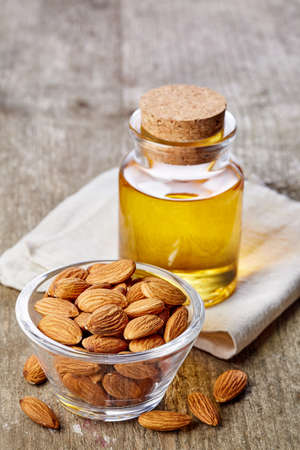 Bottle of almond oil and bowl of almonds on wooden backgroundの写真素材