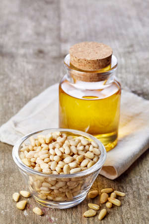 Bottle of pine nut oil and bowl of pine nuts on wooden backgroundの写真素材