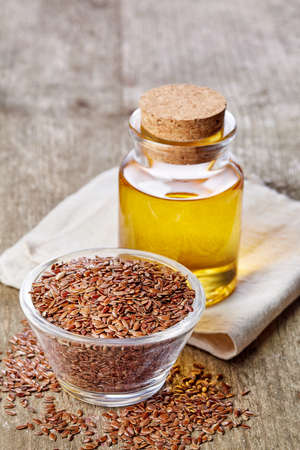 Bottle of linseed oil and bowl of linseeds on wooden backgroundの写真素材