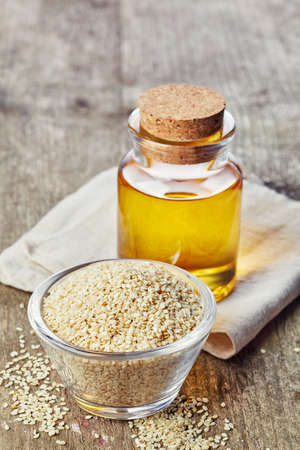 Bottle of sesame seed oil and bowl of sesame seeds on wooden backgroundの写真素材
