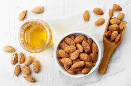 Almond oil and bowl of almonds on white wooden background. Top view