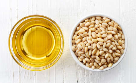 Pine nut oil and bowl of pine nuts on white wooden background. Top viewの写真素材