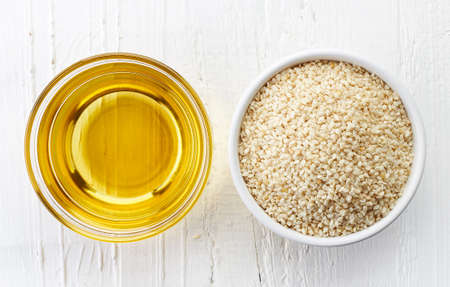 Sesame seed oil and bowl of sesame seeds on white wooden background. Top viewの写真素材