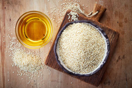Sesame seed oil and bowl of sesame seeds on wooden background. Top viewの写真素材
