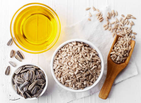 Bowl of sunflower seeds and bowl of sunflower oil on white wooden background. Top viewの写真素材