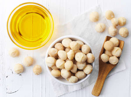 Bowl of macadamia nut oil and macadamia nuts on white wooden background. Top viewの写真素材