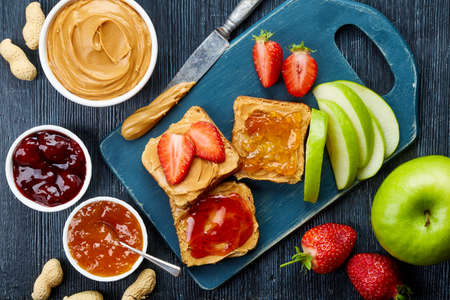 Sandwiches with peanut butter, jam and fresh fruits on dark wooden background from top viewの写真素材