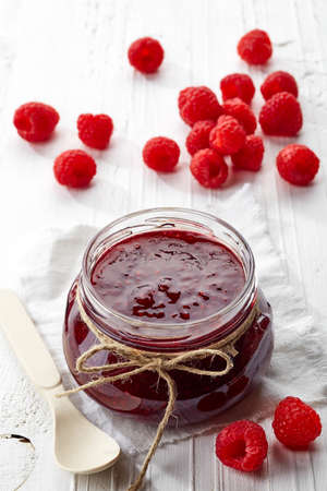 Jar of raspberry jam and fresh berries on white wooden background