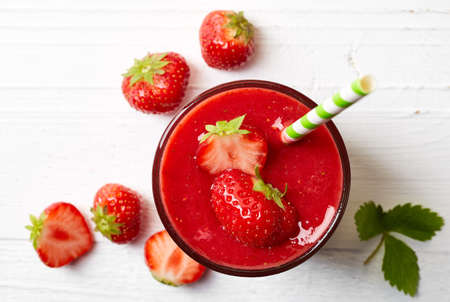 Glass of strawberry smoothie on white wooden background from top view