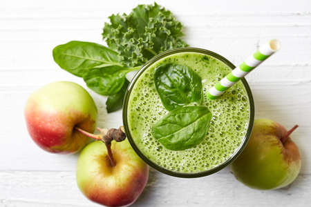 Glass of green fruit and vegetable smoothie on white wooden background from top view