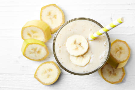 Glass of banana smoothie on white wooden background from top viewの写真素材