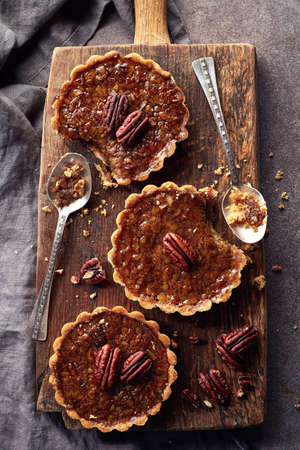 Homemade mapple syrup and pecan tarts on wooden cutting board from top viewの写真素材