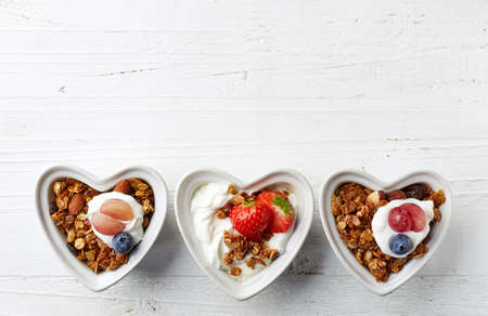 Heart shaped bowls of homemade granola and yogurt on white wooden background from top viewの写真素材