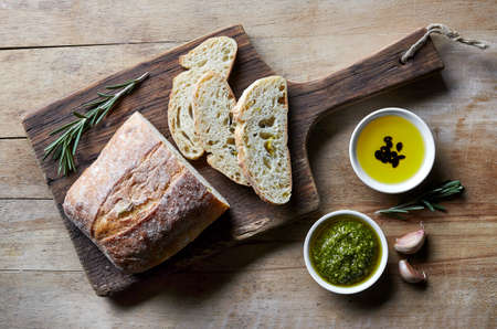 Fresh sliced italian Ciabatta bread with olive oil and pesto on wooden cutting board. From top view.の写真素材