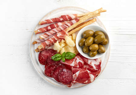 Cold smoked meat and cheese plate with olives and bread sticks on white wooden background. From top viewの写真素材