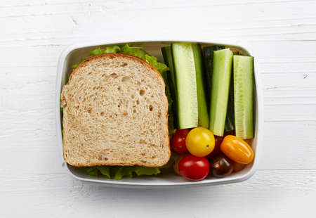 Healthy lunch box with sandwich and fresh vegetables on white wooden background. From top viewの写真素材