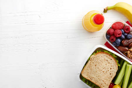 Healthy lunch boxes with sandwich, fresh vegetables, fruits and nuts on white wooden background. From top viewの写真素材