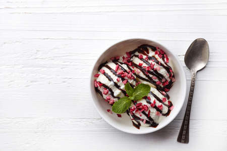 Bowl of vanilla ice cream with chocolate sauce on white wooden background. From top view