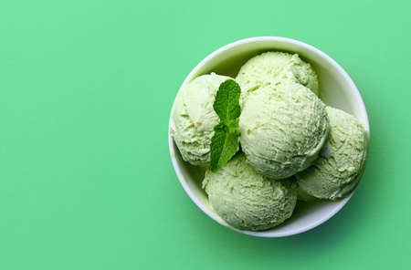 Bowl of green pistachio ice cream isolated on green background. Top view