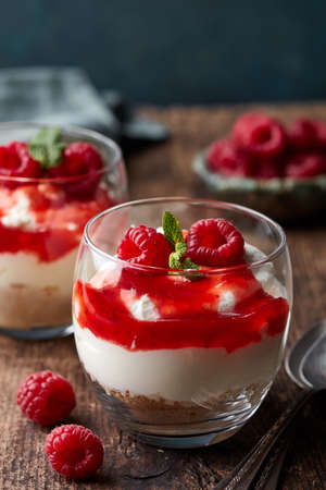 Two glasses of cheesecake with fresh berry sauce on old wooden table. Parfait dessertの写真素材