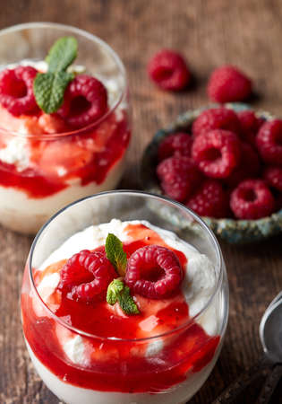 Two glasses of cheesecake with fresh berry sauce on old wooden table. Parfait dessertの写真素材