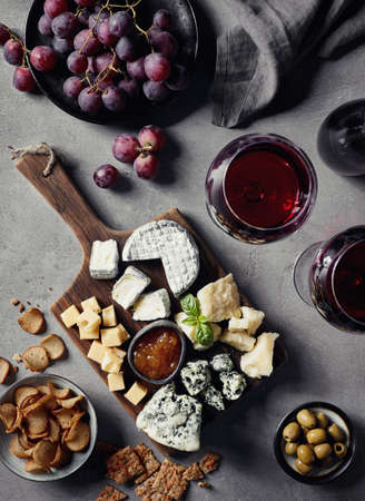 Cheese plate served with red wine, olives, grapes, jam and bread snacks on gray marble background. Top view.の写真素材