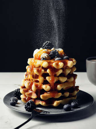 Plate of belgian waffles with whipped cream, caramel sauce, fresh berries and falling powdered sugarの写真素材