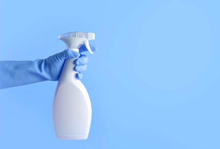 Hand with rubber glove holding white spray bottle on blue background