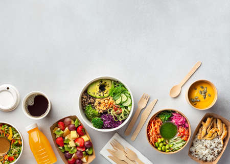 Healthy take away food and drinks in disposable eco friendly paper containers on gray background, top view. Fresh salad, soup, poke bowl, buddha bowl, fruits, coffee and juice.