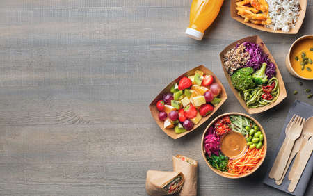 Healthy take away food and drink in disposable eco friendly paper containers on gray wooden background, top view. Fresh salad, soup, poke bowl, vegetable, fruits, chicken wrap and juice.の写真素材